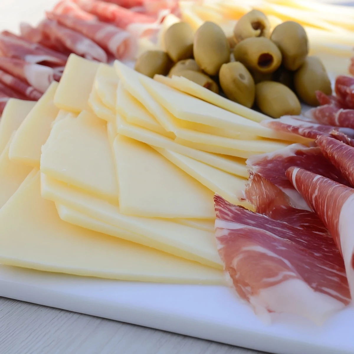A gourmet close-up of the Minimalism Master: arranged cheese, ham, and olives on a board.