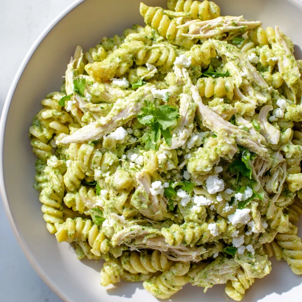 Creamy cilantro lime chicken pasta with shredded chicken and rotini in a tangy yogurt sauce, garnished with cotija and lime wedges.