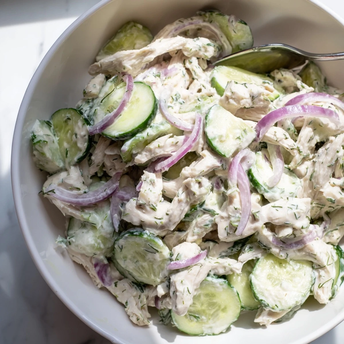 A close-up of creamy cucumber chicken salad in a rustic bowl, with shredded chicken and crisp cucumber slices coated in a dill yogurt dressing.  