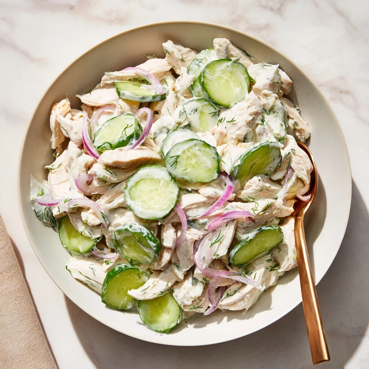 Chilled creamy cucumber chicken salad served in a clear glass bowl, garnished with fresh dill and sliced green onions.