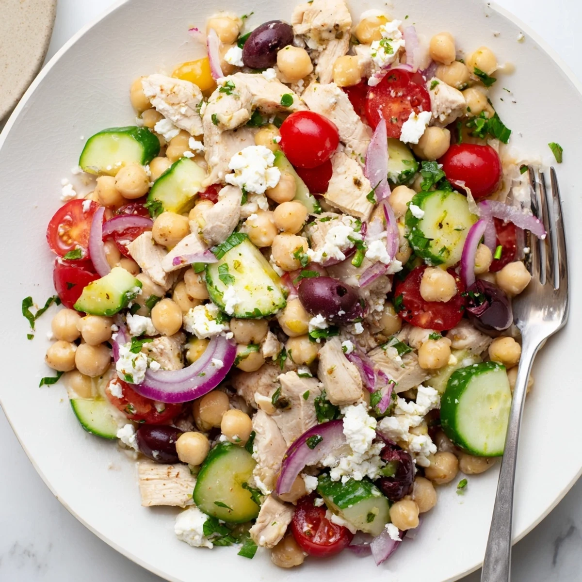 Colorful Mediterranean Chickpea Chicken Salad featuring juicy chicken, creamy feta, crisp vegetables, and briny olives, served on a rustic wooden board.