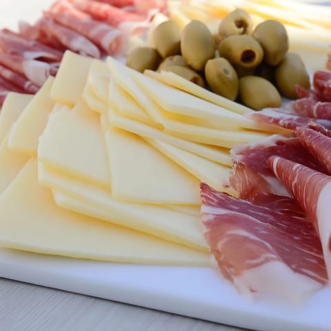 A gourmet close-up of the Minimalism Master: arranged cheese, ham, and olives on a board.