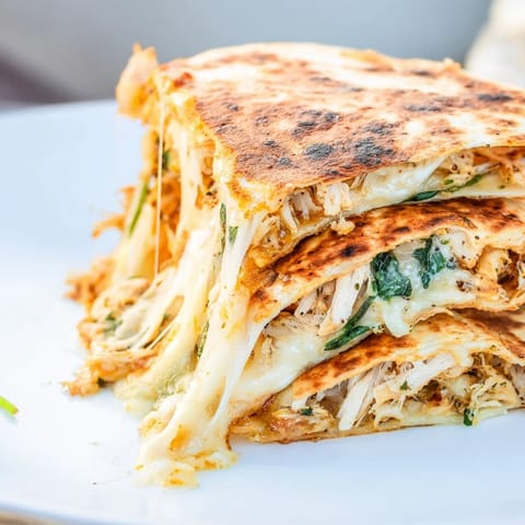 Close-up of a homemade Chicken and Spinach Quesadilla slice, revealing tender chicken, wilted spinach, and gooey cheese tucked inside a soft flour tortilla.  