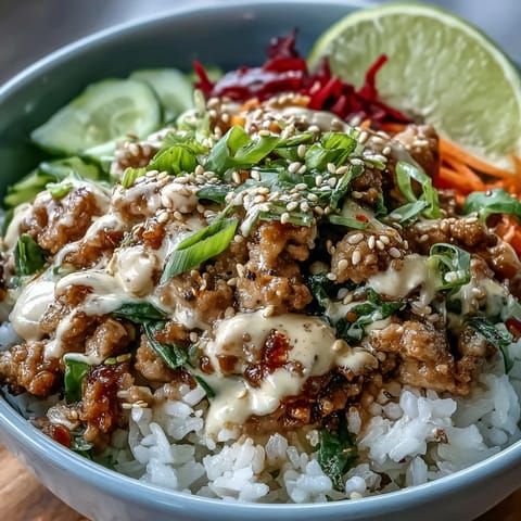 A close-up of Bang Bang Ground Turkey Rice Bowls shows lime wedges, sesame seeds, and colorful carrots, cucumber, and cabbage toppings.