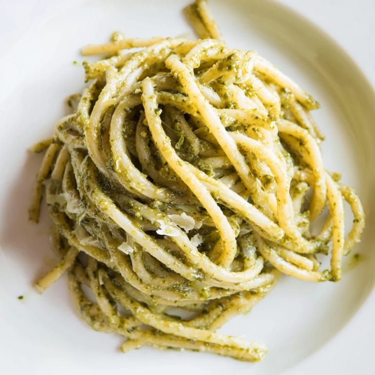 A close-up of creamy sunflower seed pesto pasta topped with fresh basil and grated Parmesan, served alongside a crisp salad.  